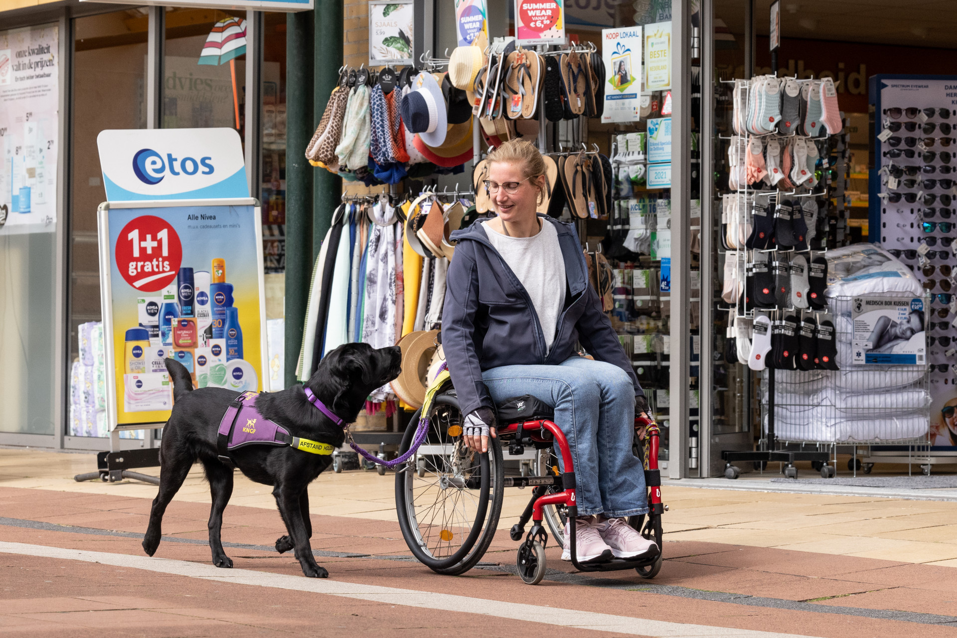 Nynke in haar rolstoel in een winkelstraat, Jissa loopt naast haar